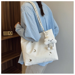 Detail of white tote bag featuring metallic butterfly studs and a plush cloud charm