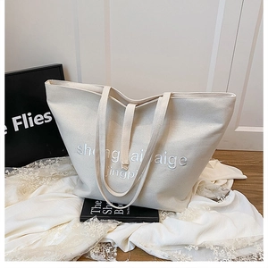 Vue détaillée du grand sac cabas en toile avec broderie de lettres et large bandoulière