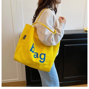 Model view of a large yellow canvas tote bag with bag text and fashion label