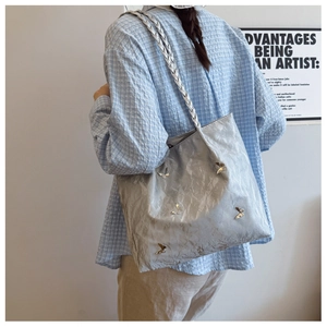 Detail of silver tote bag with crinkled texture, butterfly buckles, and woven strap