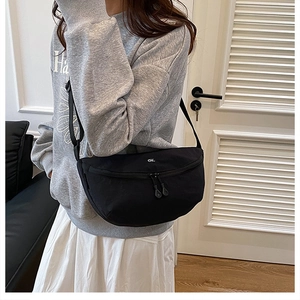 Detail of black nylon half-moon crossbody bag featuring white ok embroidery and double zippers