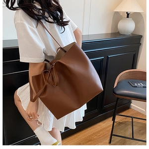 Close-up of minimalist brown leather tote bag with stylish side strap detail on a model