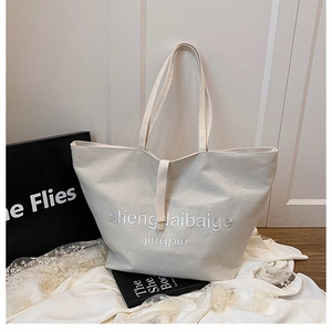 Détail du sac cabas en toile beige avec broderie blanche et poignée verticale stylée