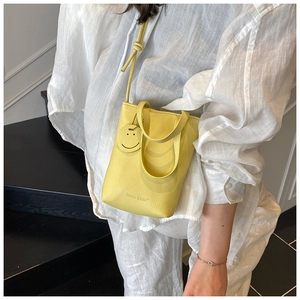 Close-up of yellow lychee grain leather handbag with a smiley face charm and logo detail
