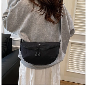 Detail of black nylon dumpling bag with OK logo and dual zipper on model with grey hoodie