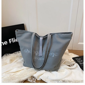 Détail du cabas en toile grise avec poignées renforcées et lettrage brodé sur le sac
