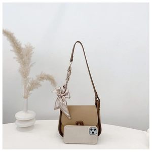 Detail of minimalist beige handbag with brown buckle and decorative silk scarf accessory