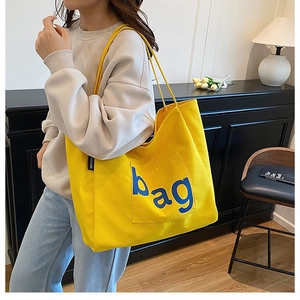 Detail of yellow canvas tote bag with blue 'bag' lettering and fashion tag on shoulder