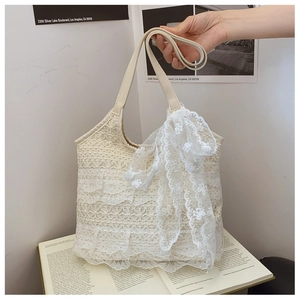 Detailed texture of cream lace tote bag with floral patterns and a large ribbon bow