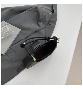 Detail der schwarzen Achseltasche mit gewebtem Knotengriff und goldenen Metallteilen
