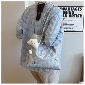 Detail of silver crinkled tote bag with metal butterfly accents and plush cloud charm