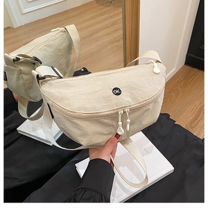 Close-up of beige nylon crescent bag with double zipper and 'ok' circular patch logo