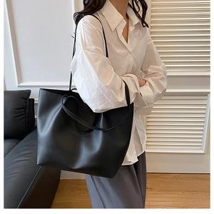 Close-up of minimalist black leather tote bag showing smooth matte finish and slim straps