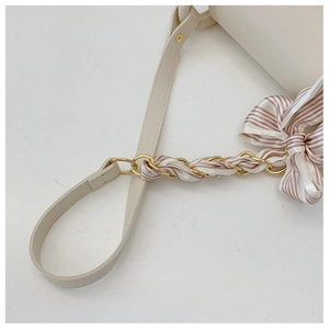Detail of off-white shoulder bag with golden chain and silk scarf bow on strap