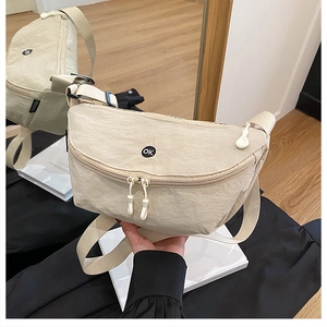 Detail of beige nylon crossbody bag featuring a circular OK patch and resin zippers
