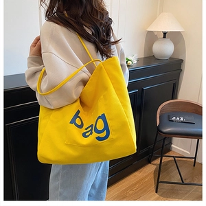 Detailed view of bright yellow canvas tote bag with bold blue bag lettering on model