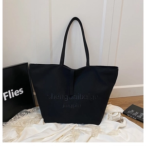 Détail du grand sac cabas noir en toile avec lettrage en relief sur un tissu de dentelle blanche