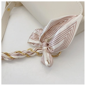 Close-up of beige leather bag with stylish striped silk scarf tied on chain strap