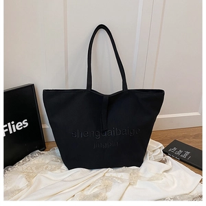 Détail du grand sac cabas en toile noire avec lettrage embossé et longues anses d'épaule