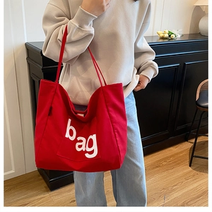 Fashionable red canvas tote bag with bold white 'bag' lettering on a stylish model