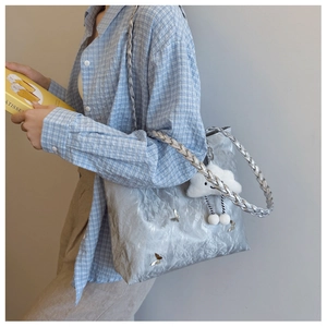 Detail of silver pleated tote bag with woven strap and butterfly charm worn by a model