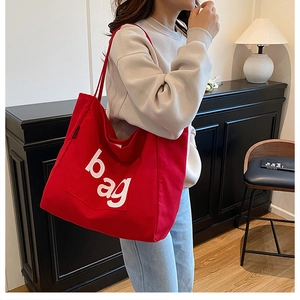 Detailed view of a red canvas tote bag with a white 'bag' print and handy front pocket