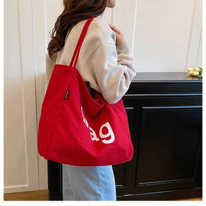 Red canvas tote bag with white Bag print being worn by a model in a minimalist interior