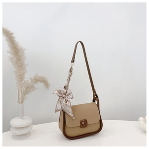 Detail view of khaki crossbody bag with silk scarf on white table with minimalist decor