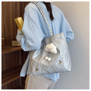 Detail of silver metallic tote bag featuring gold butterfly charms and cloud pendant
