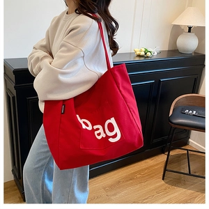 Detail of red canvas tote bag with white bag lettering and fashion tag on strap