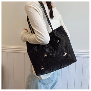 Detail of black tote bag with butterfly metal accents and woven shoulder straps