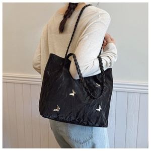 Detail of black pleated tote bag with silver butterfly charms worn by a model