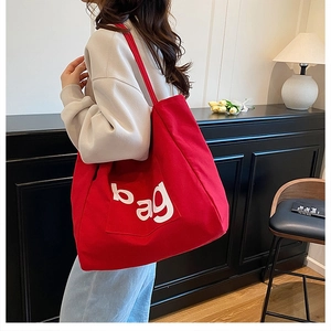 Detail of red canvas tote bag featuring white bag letters and a front pocket for storage