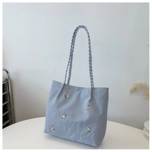 Detail of light blue tote bag with unique pleated texture and metal butterfly accents