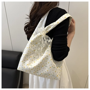 Detail of floral canvas shoulder bag with a white lace bow on the strap worn by model
