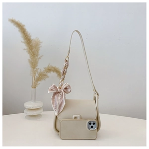 Close-up of a cream-colored crossbody bag with a decorative silk scarf and a phone for size