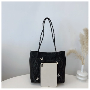 Detailed view of a black tote bag with silver butterfly charms and a tablet for scale