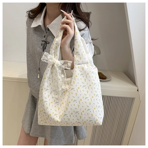 Detail of canvas tote bag with yellow floral print and a large white lace bow accent