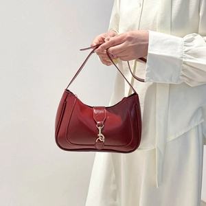Borsa hobo bordeaux lucida con fibbia dorata portata a spalla su sfondo bianco neutro