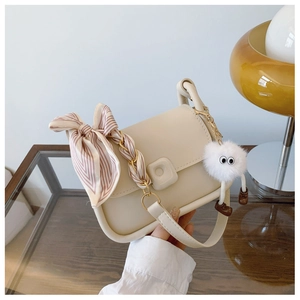 Detail of off-white PU leather handbag with silk scarf and cute plush pendant