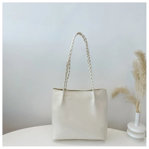 Detail of hand-woven dual handles on a minimalist cream-white leather tote bag