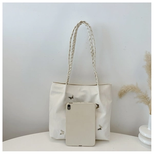 Detail of cream white tote bag with woven handles and decorative metal butterfly accents
