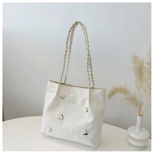 Detail of a white minimalist tote bag featuring silver metal butterfly charms and woven handles