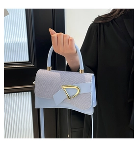 Detail of light blue crossbody bag featuring woven texture flap and gold D-shaped buckle