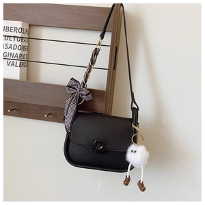 Detail of matte black shoulder bag with ribbon bow, chain strap and quirky plush pendant