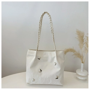 Close-up of white tote bag with metallic butterfly accents and braided handles