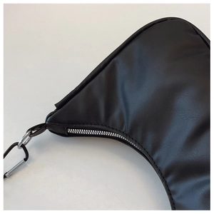 Detail of black crescent shoulder bag featuring silver metal zipper and carabiner charm