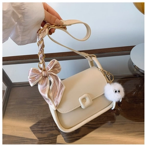 Detail of cream flap bag with silk scarf bow and fluffy pompom charm accessory
