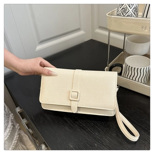 Détail de la texture tissée beige et du rabat rectangulaire sur cette pochette chic