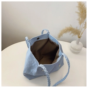 Detail view of light blue tote with braided handles and metal bear charm accent